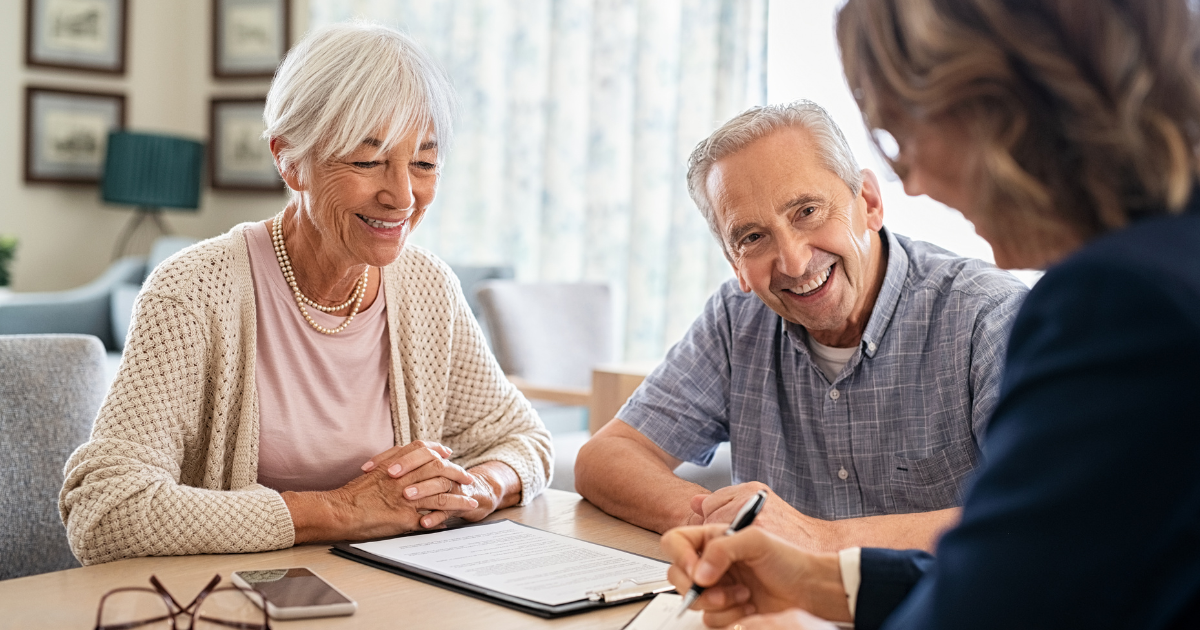 Smiling senior couple sitting at a table with a care coordinator while reviewing home care service documents together.