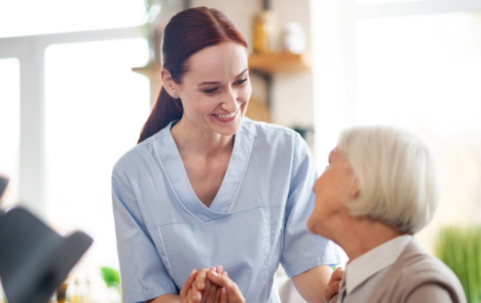 Smiling caregiver holding hands with an elderly woman during a warm and supportive in-home care visit.