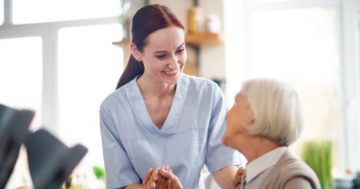 Smiling caregiver holding hands with an elderly woman during a warm and supportive in-home care visit.