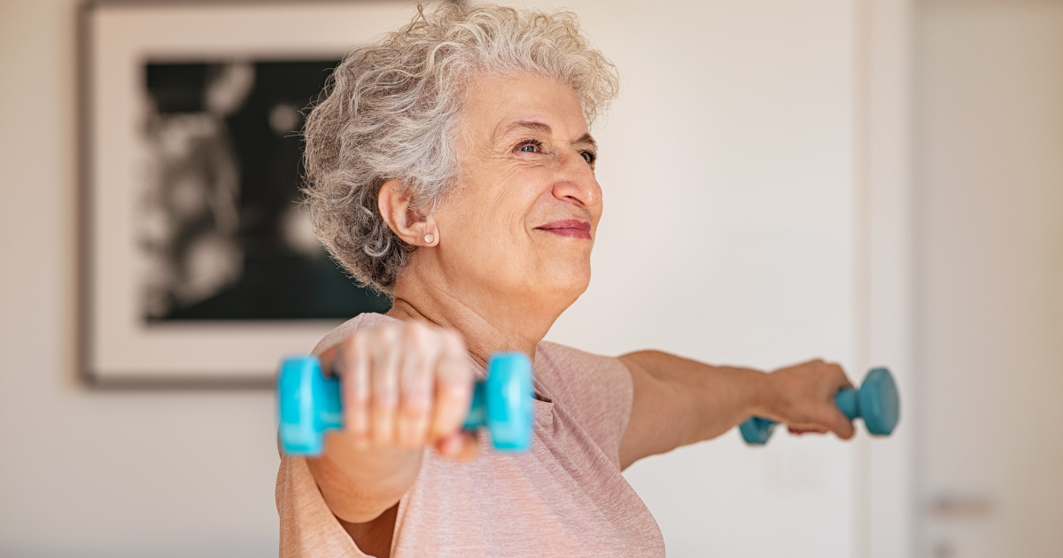 Smiling senior woman exercising with light dumbbells at home to improve strength, balance, and mobility.