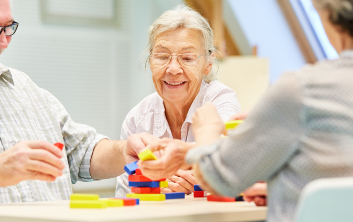 Group of seniors smiling and playing a colorful stacking game together at a table during an in-home care activity.