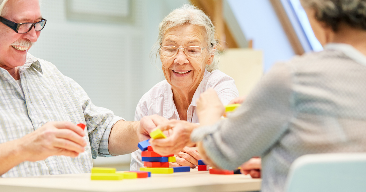 Group of seniors smiling and playing a colorful stacking game together at a table during an in-home care activity.