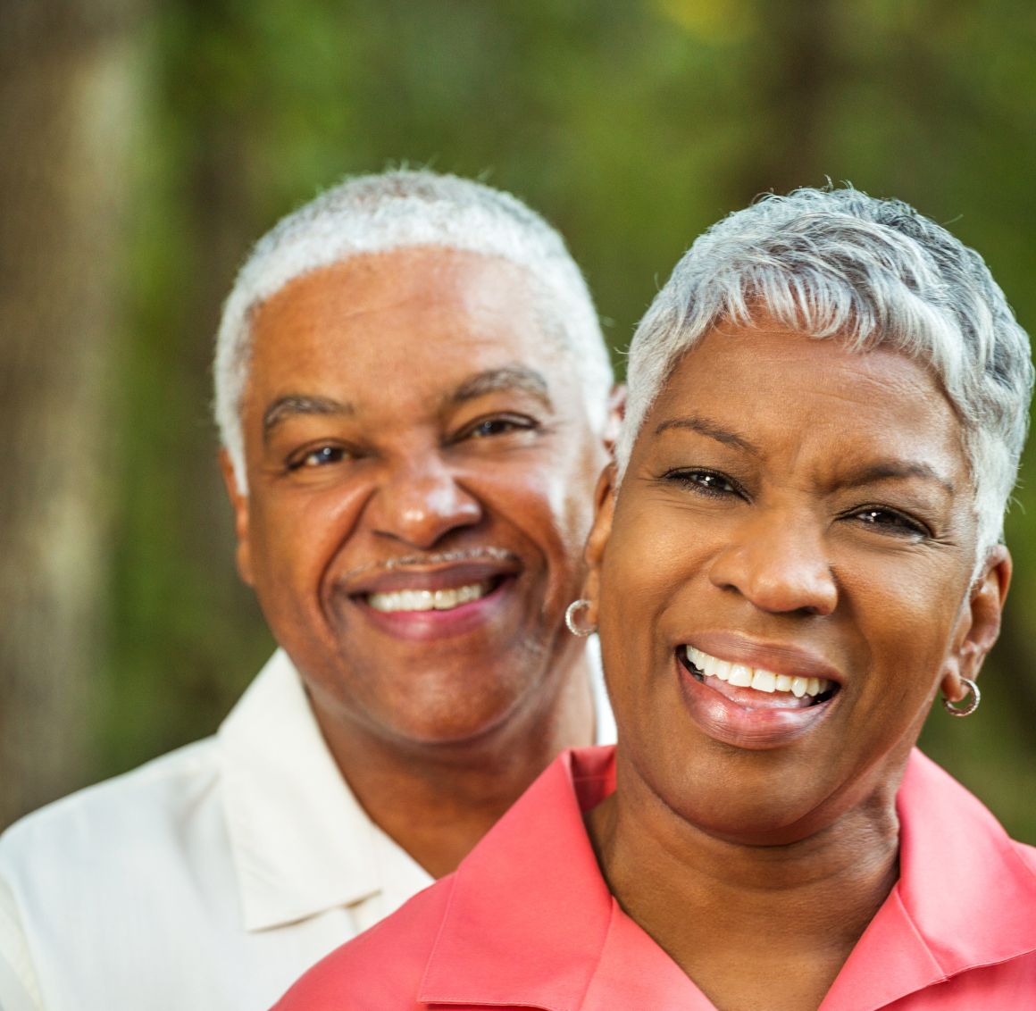Happy Senior Couple Smiling Together Outdoors in a Peaceful Natural Setting Smiling senior couple standing closely together outdoors with green trees in the background